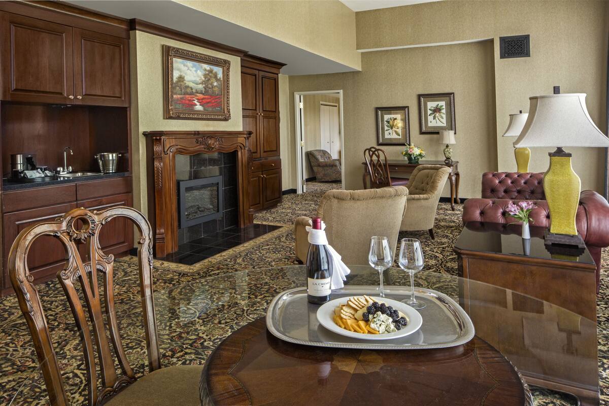 A dining area with a table set for two, featuring a tray with a bottle, glasses, and a plate of food.