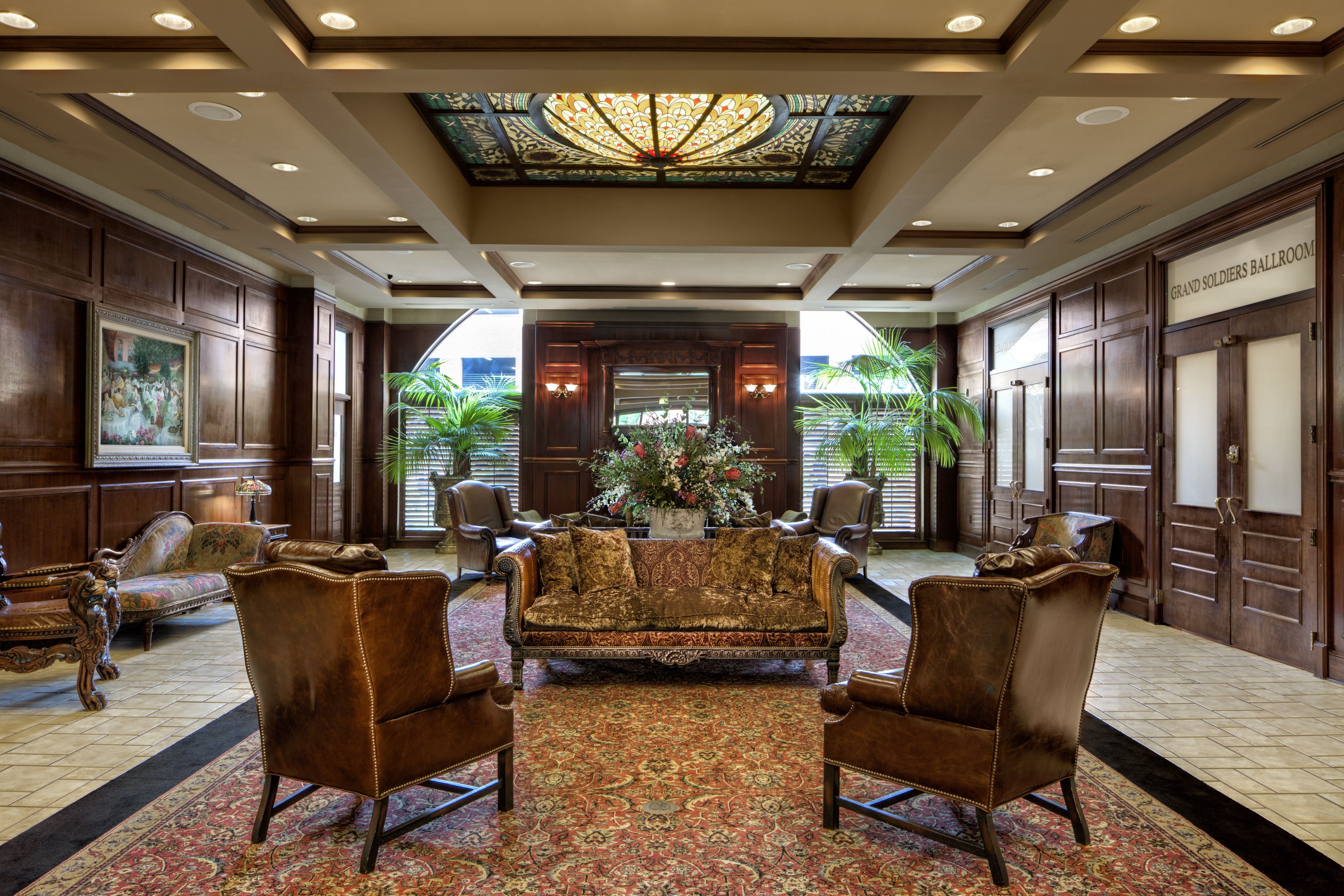 A grand lobby with a large, ornate chandelier, a central floral arrangement, and a sofa with matching armchairs.
