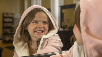 A child in a pink hoodie looking at their reflection in a mirror.