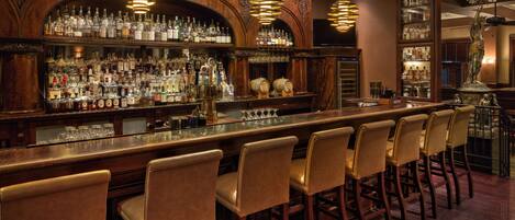 A bar with multiple liquor bottles, a long counter, and several bar stools.