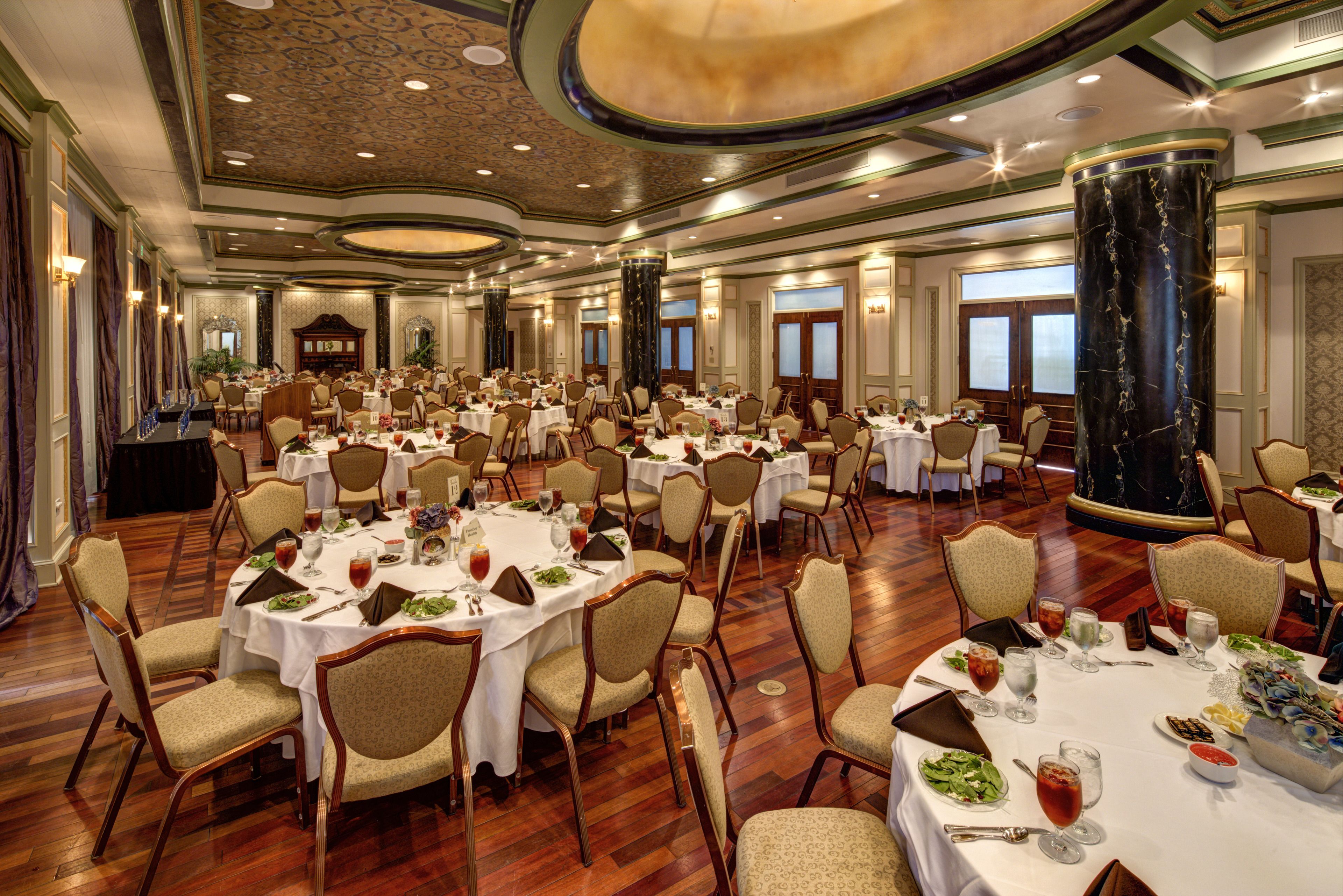 A banquet hall with round tables, chairs, and a large central column.