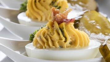 A row of deviled eggs garnished with bacon and parsley, served on white spoons.