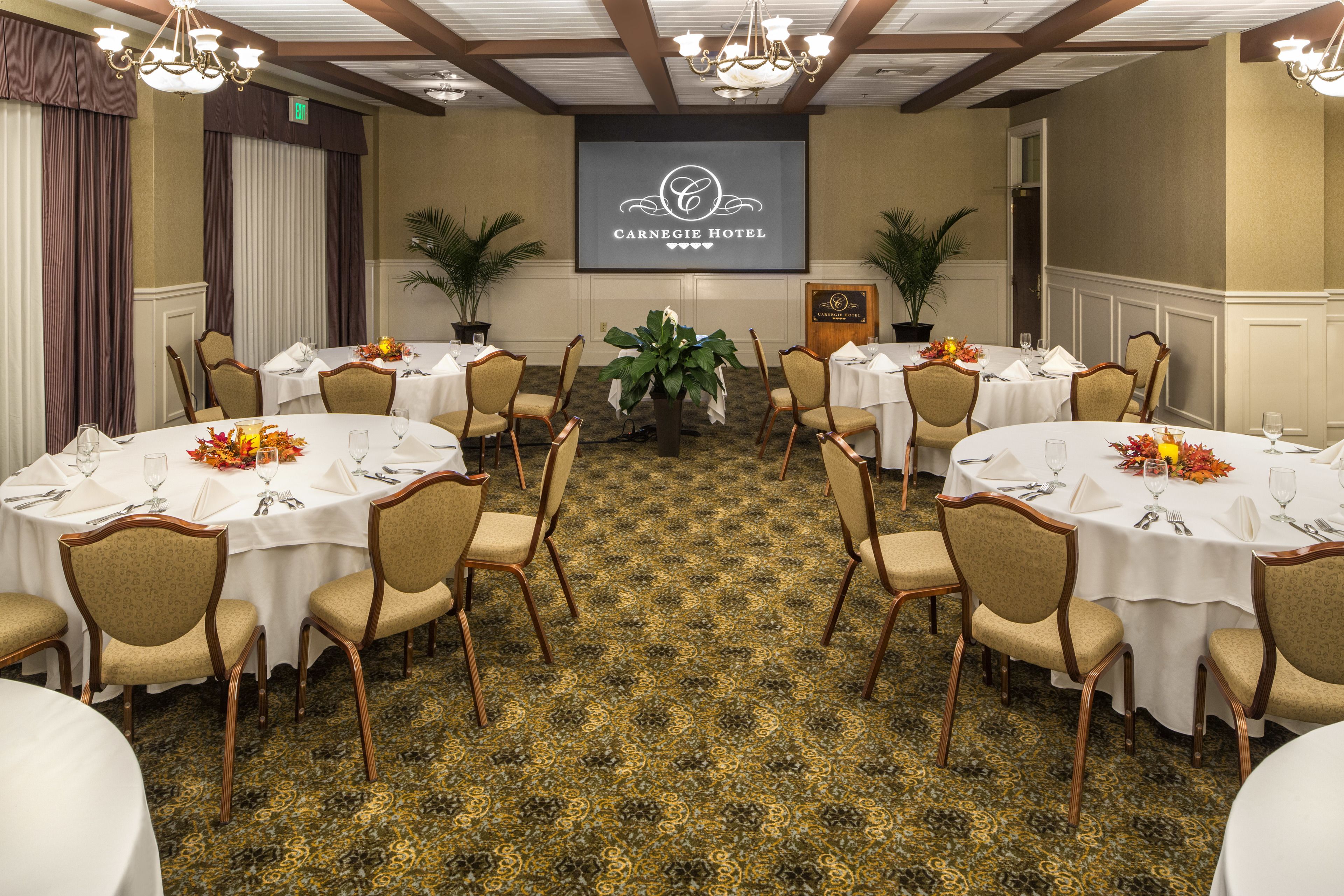 A conference room at the Carnegie Hotel with round tables, chairs, and a carpeted floor.