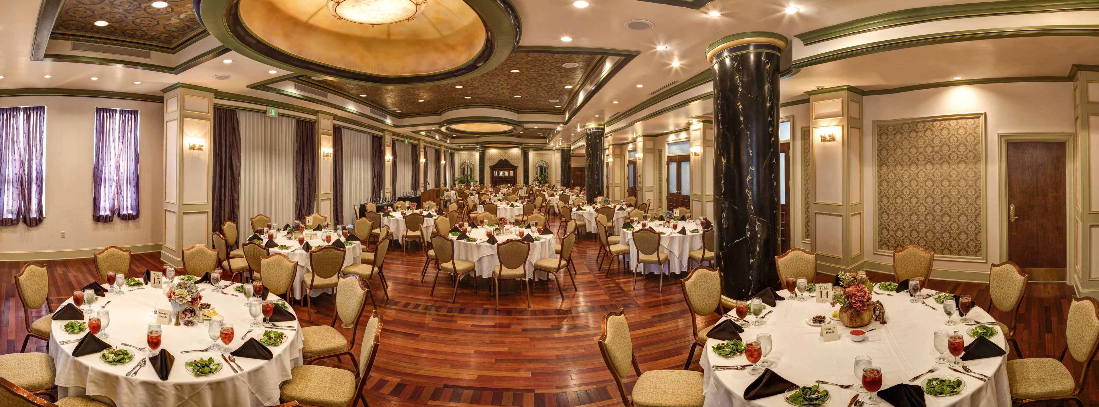A large banquet hall with multiple round tables, each set with white tablecloths, chairs, and centerpieces.