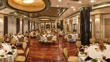 A large banquet hall with multiple round tables, each set with white tablecloths, chairs, and centerpieces.