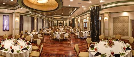 A large banquet hall with multiple round tables, each set with white tablecloths, chairs, and centerpieces.