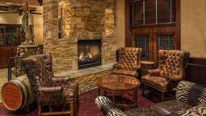 A cozy lounge area with leather armchairs, a round wooden table, and a stone fireplace. - Carnegie Hotel & Spa (Johnson City)