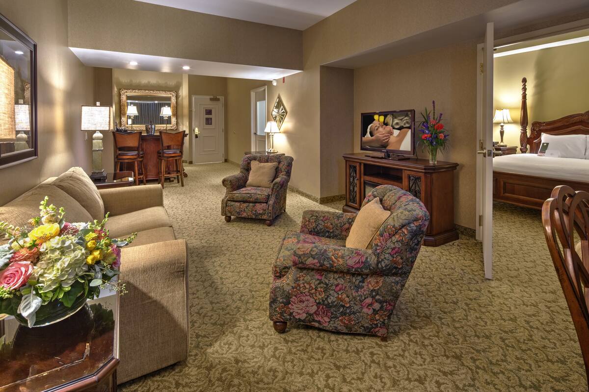 A hotel room with a large bed, two armchairs, a sofa, a TV, a desk with a lamp, and a mirror.