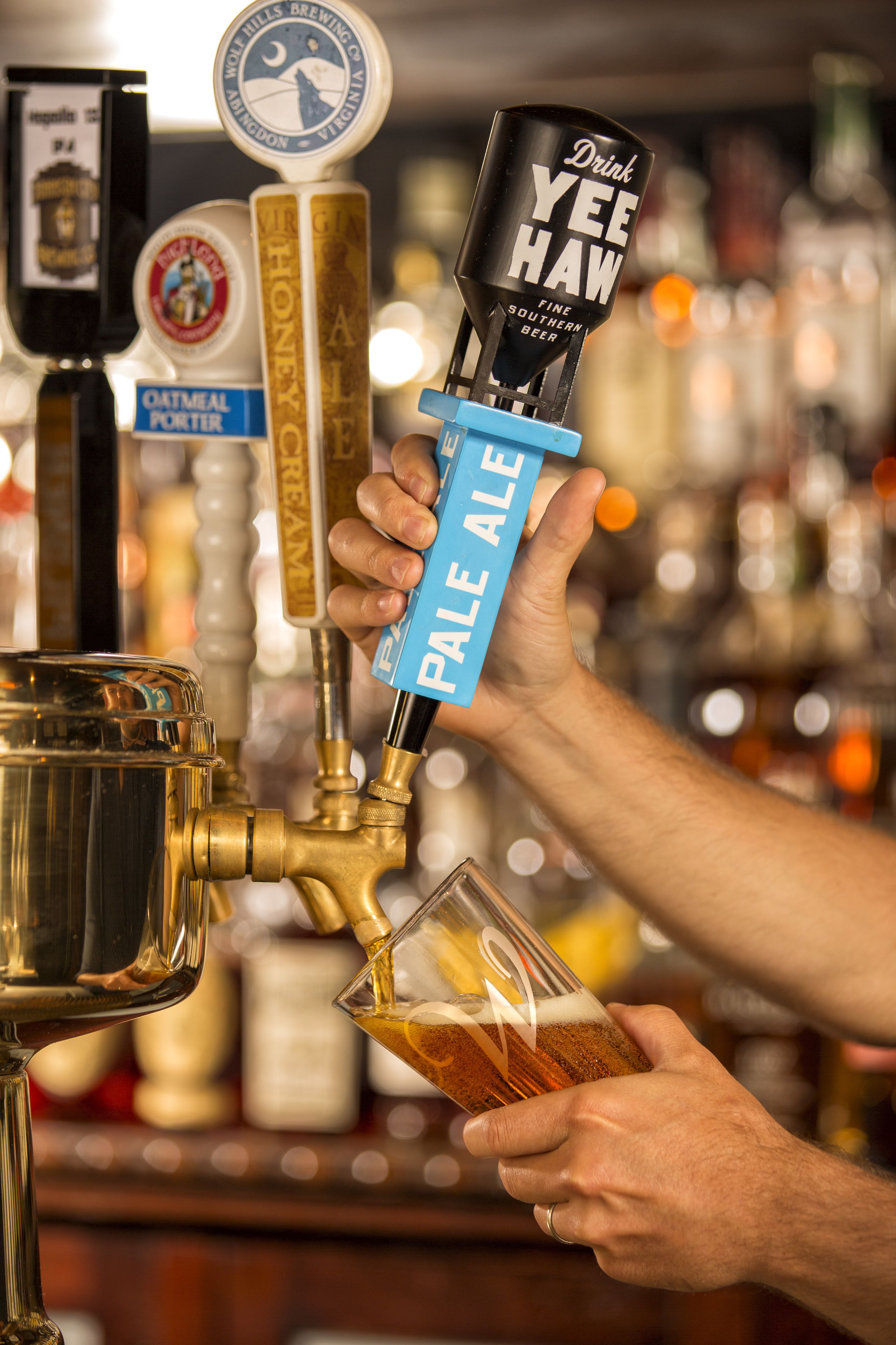 A person pouring pale ale beer from a tap labeled "Drink Yee Haw" into a glass.