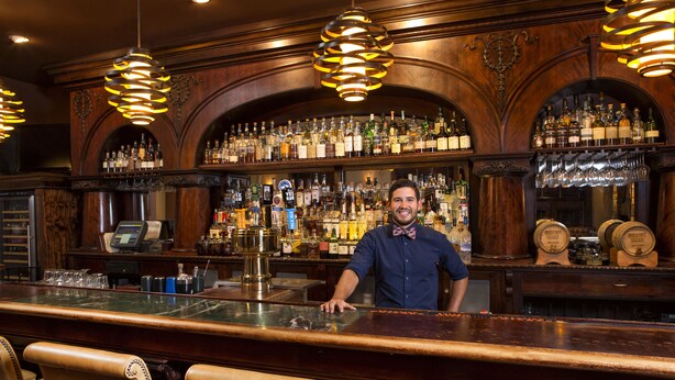 A bar with wooden decor, multiple liquor bottles, and a bartender. - Carnegie Hotel & Spa (Johnson City)