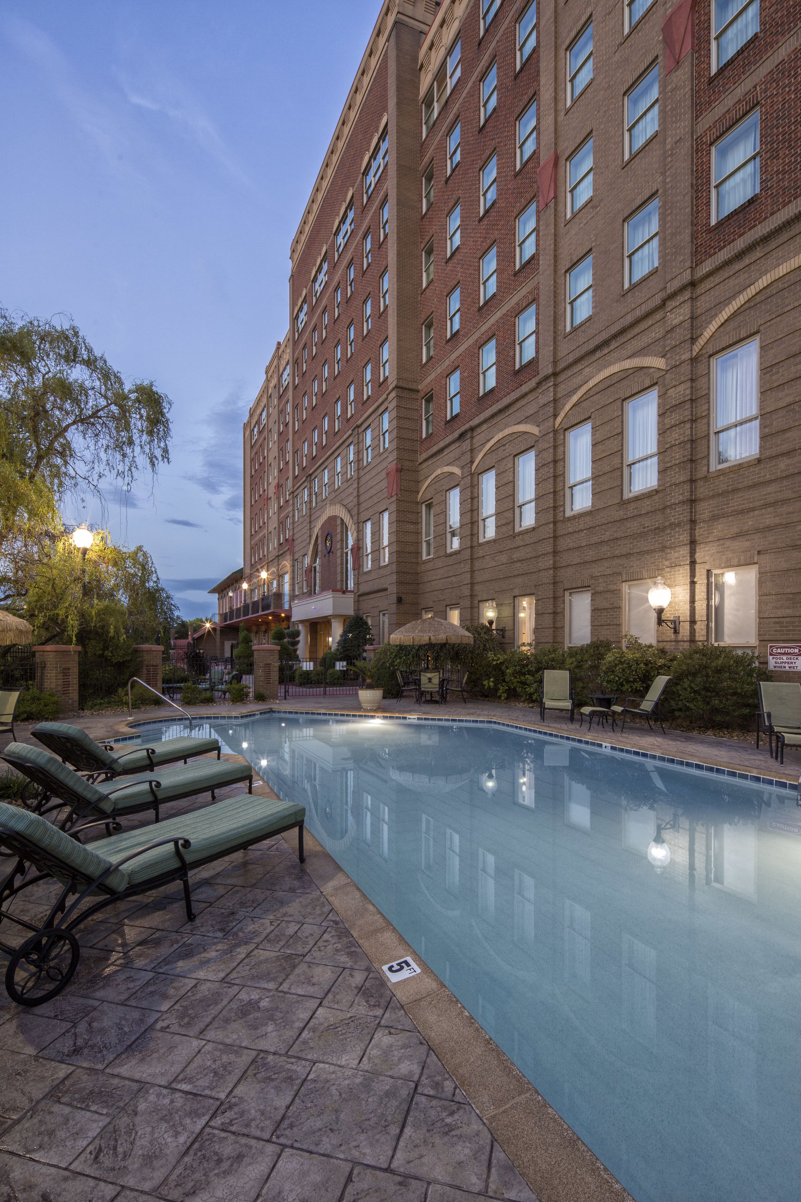 A hotel with a swimming pool, lounge chairs, and a brick facade.