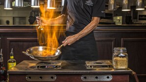 A chef cooking with a wok on a stove, a jar of spices, and a bottle of oil on the counter. - Carnegie Hotel & Spa (Johnson City)