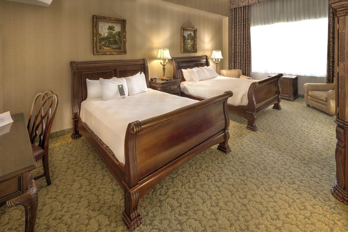A hotel room with two wooden beds, a chair, a desk, and a large window.