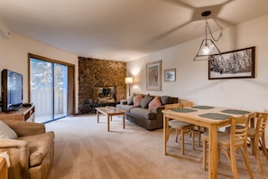 A living room with a stone fireplace, a television, a sofa, a dining table with chairs, and a large window.