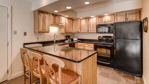 A modern kitchen with wooden cabinets, a black refrigerator, and a central island with chairs. - Westwind at Vail (Vail)