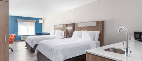 Quarto de hotel com duas camas, pia branca e uma escrivaninha com computador.