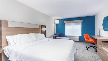 A modern hotel room with a large bed, a desk, an orange chair, and a blue accent wall.