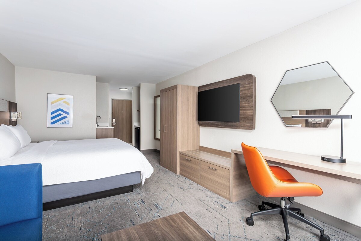 Een hotelkamer met een bed, een bureau, een oranje stoel, een grote spiegel en een televisie.