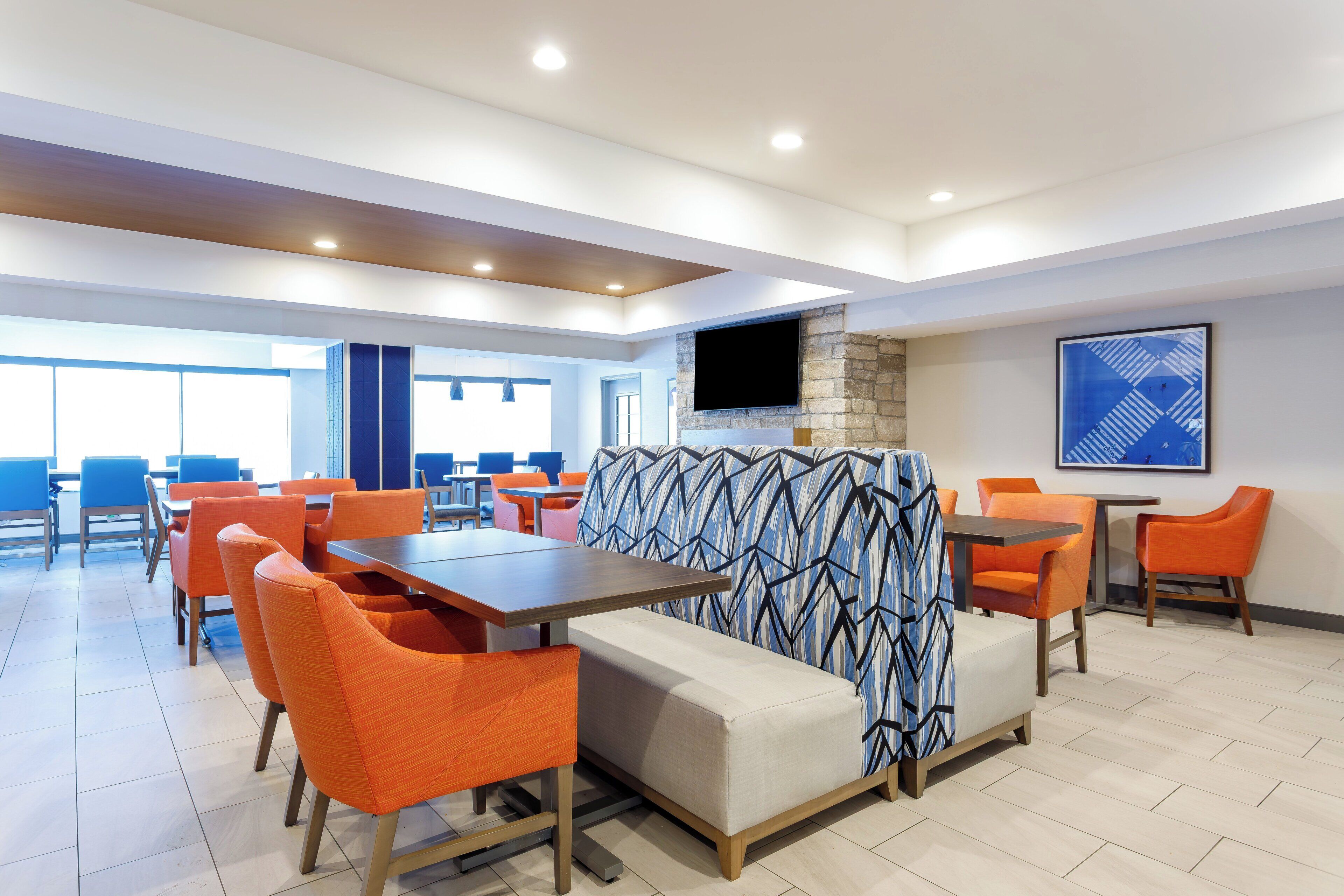 A modern dining area with orange chairs, a sofa, and a TV mounted on a stone wall.