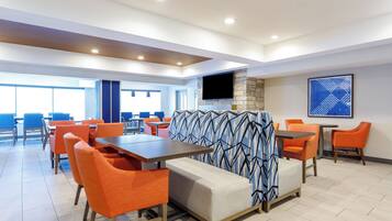 A modern dining area with orange chairs, a sofa, and a TV mounted on a stone wall.