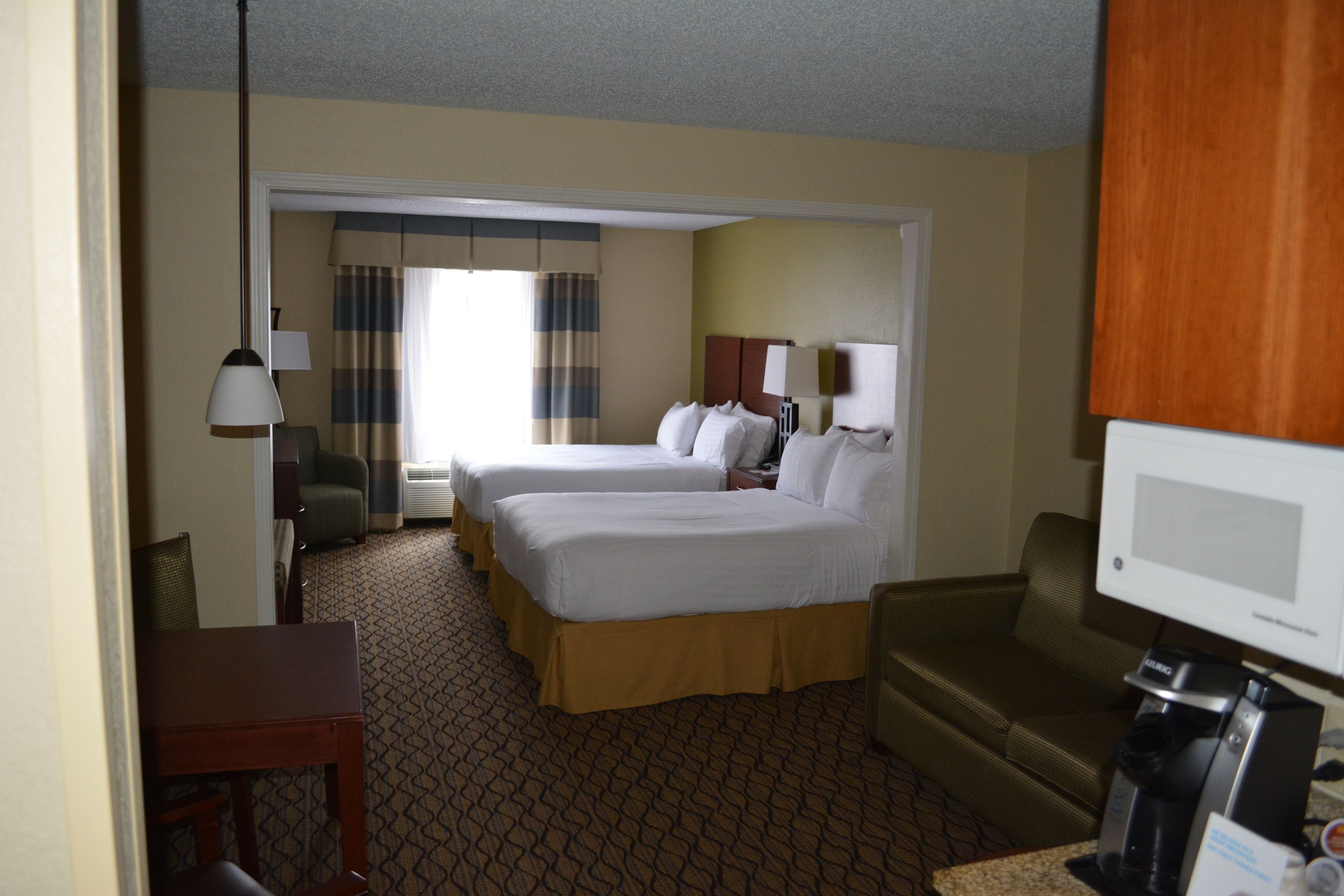 A hotel room with two beds, a desk, a chair, a television, and a coffee maker.