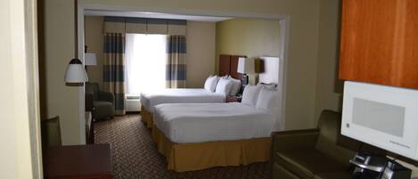 A hotel room with two beds, a desk, a chair, a television, and a coffee maker.