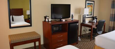 A hotel room with a bed, a desk with a computer, a television, a microwave, and a small bench.
