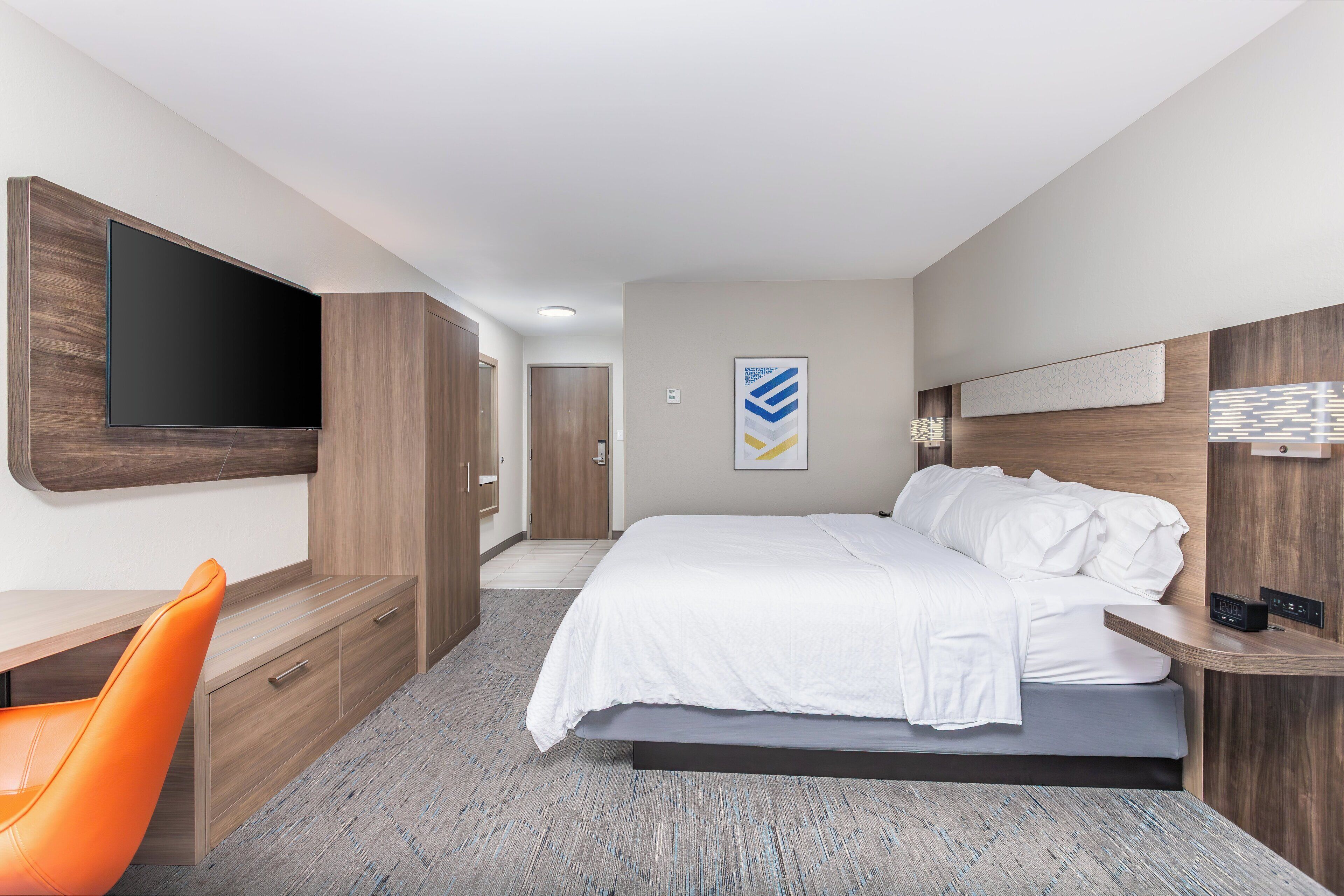 Una habitación de hotel moderna con una cama, un escritorio, una silla y un televisor montado en la pared.