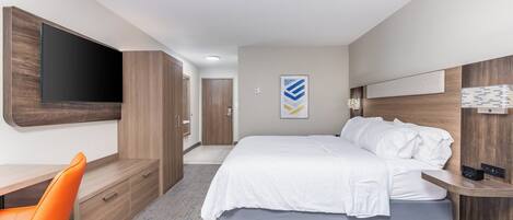 A modern hotel room with a bed, a desk, a chair, and a TV mounted on the wall.