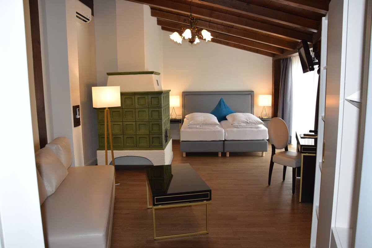 Une chambre d’hôtel comprenant un lit, deux tables de chevet, un bureau, une chaise, une armoire verte et un lustre.