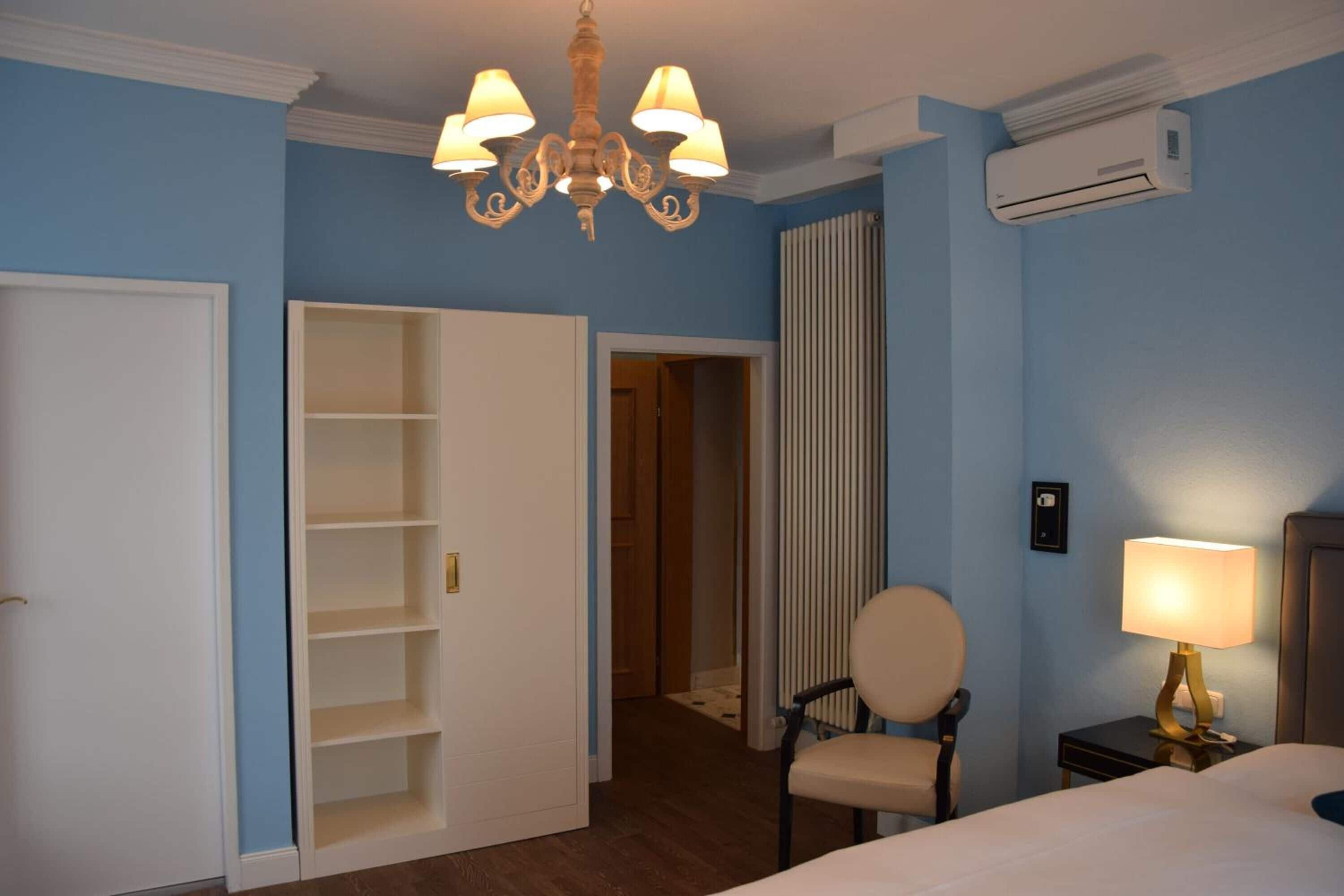 Ein Hotelzimmer mit Bett, Sessel, Nachttisch mit Lampe, Kleiderschrank und Klimaanlage.