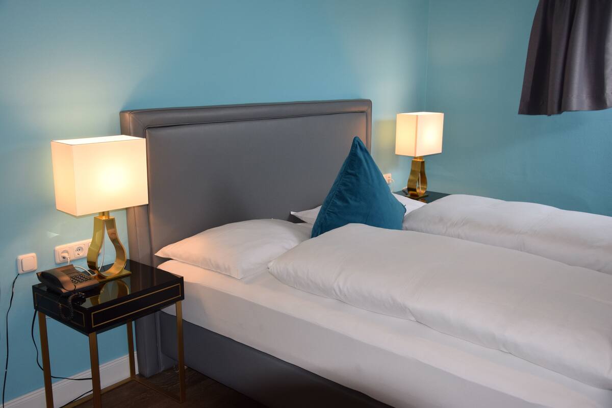 Une chambre d’hôtel équipée d’un lit, de deux lampes de chevet, d’un téléphone et d’une prise électrique.
