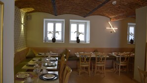 Comedor con mesas y sillas de madera, techo alto con vigas a la vista y ventanas decoradas con macetas.