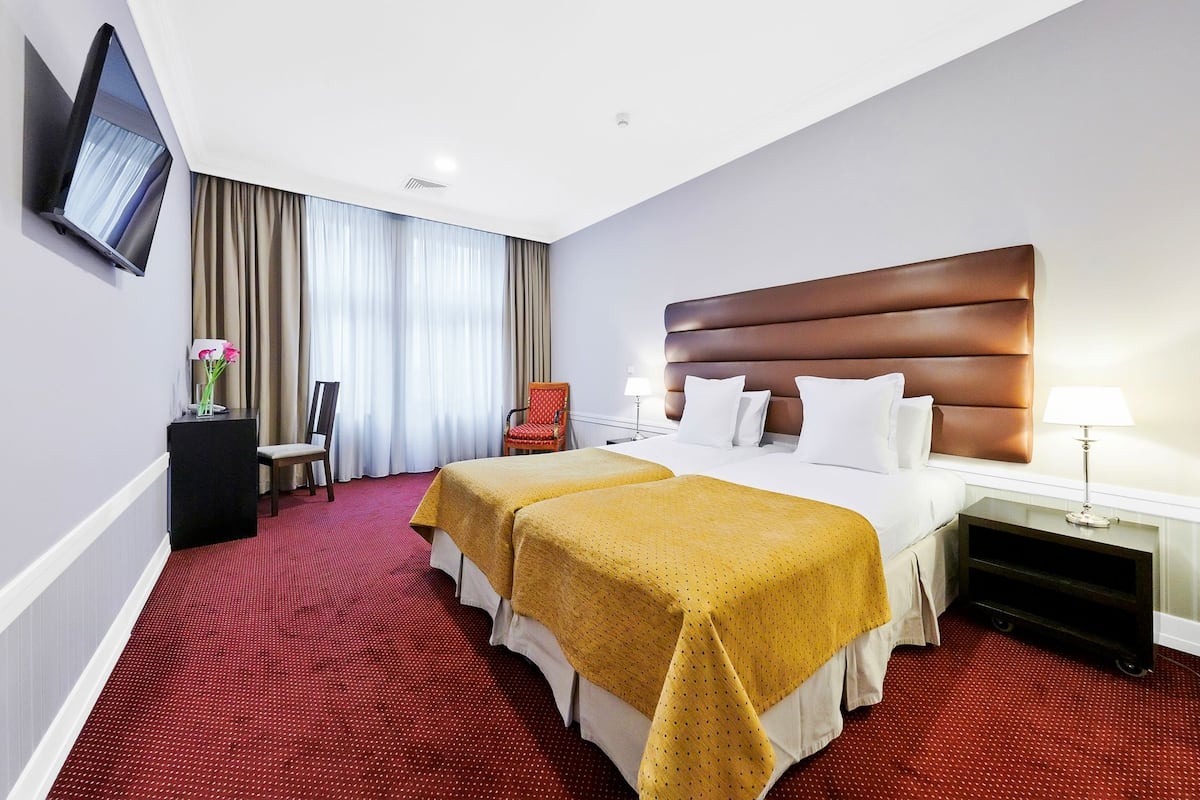 Habitación de hotel con dos camas, un televisor montado en la pared, un escritorio con lámpara y una silla.