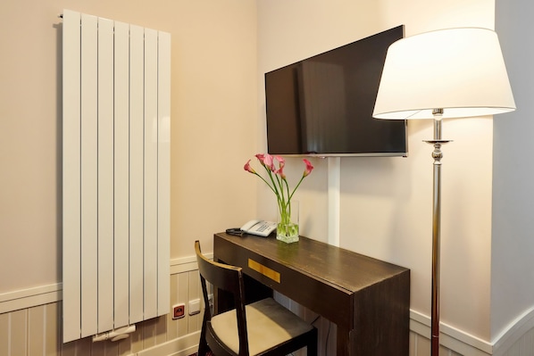 Habitación de hotel con un escritorio de madera, una silla, una lámpara, un televisor de pantalla plana y un radiador.