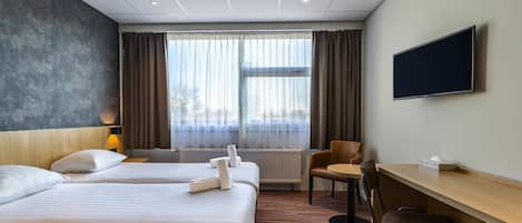 Habitación de hotel con dos camas, un escritorio, una silla, un televisor y una ventana con cortinas.