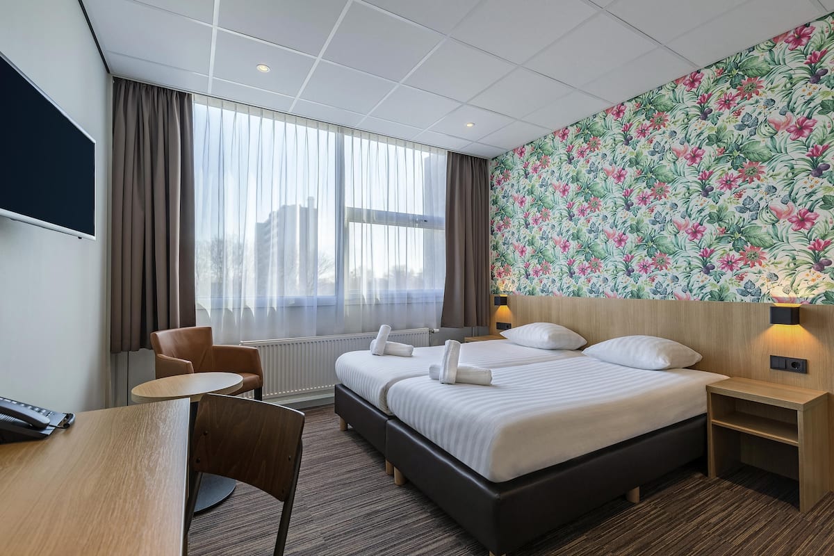 A hotel room with a large bed, a desk, a chair, a TV, and a floral wallpaper.