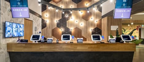 A reception desk with multiple check-in kiosks, a wall with geometric patterns, and multilingual welcome signs.