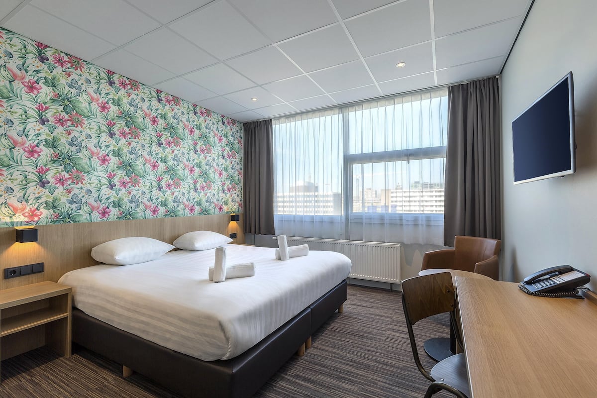 A hotel room with a large bed, a desk, a chair, a TV, and a window with curtains.