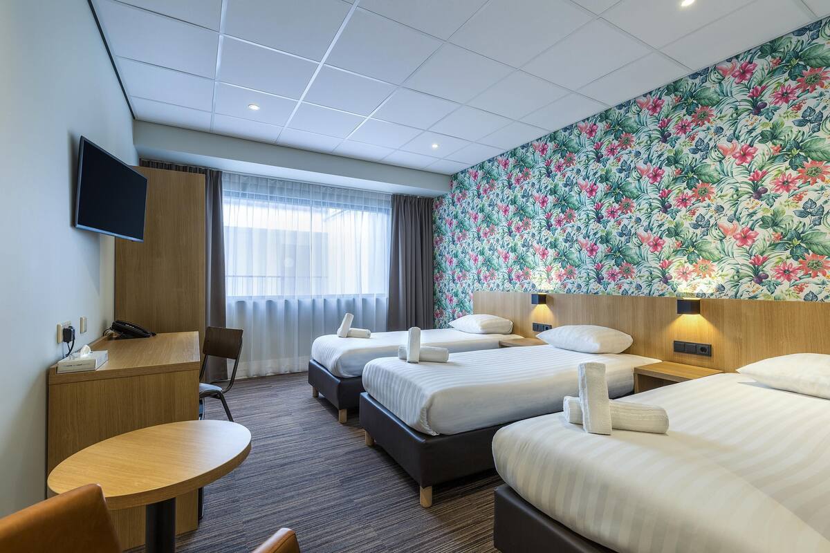 A hotel room with three beds, a desk, a chair, and a TV.