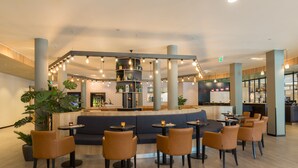 Un espacio interior moderno con una zona de estar central, varias mesas y una barra.