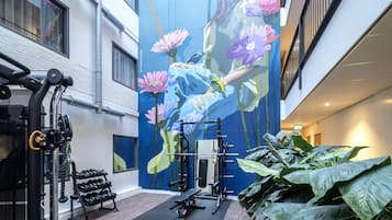 A gym with exercise equipment and a large mural of flowers and birds.