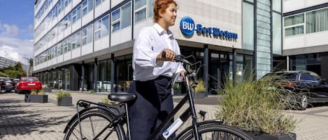 A person on a bicycle in front of a building with a sign that reads 'BW Best Western.'