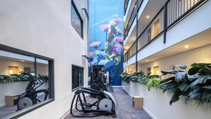 Un pasillo moderno de hotel con equipo de ejercicio, ventanas amplias y plantas de interior.
