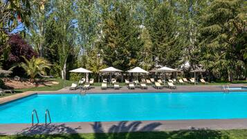 A swimming pool with lounge chairs and umbrellas, surrounded by trees and greenery.