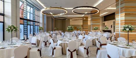 Un salón de banquetes con mesas redondas, sillas blancas y centros de mesa florales.