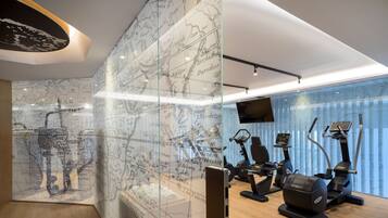 Uma academia moderna com equipamentos de exercício, um grande mural de um mapa-múndi e uma televisão na parede.