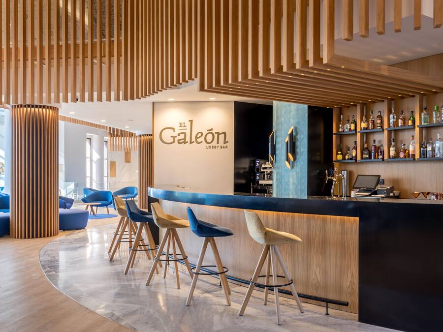 Un moderno vestíbulo con zona de bar, techo de listones de madera y taburetes de bar azules.
