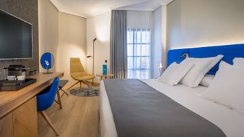 Habitación de hotel con cama, escritorio, silla, televisor y ventana con cortinas.
