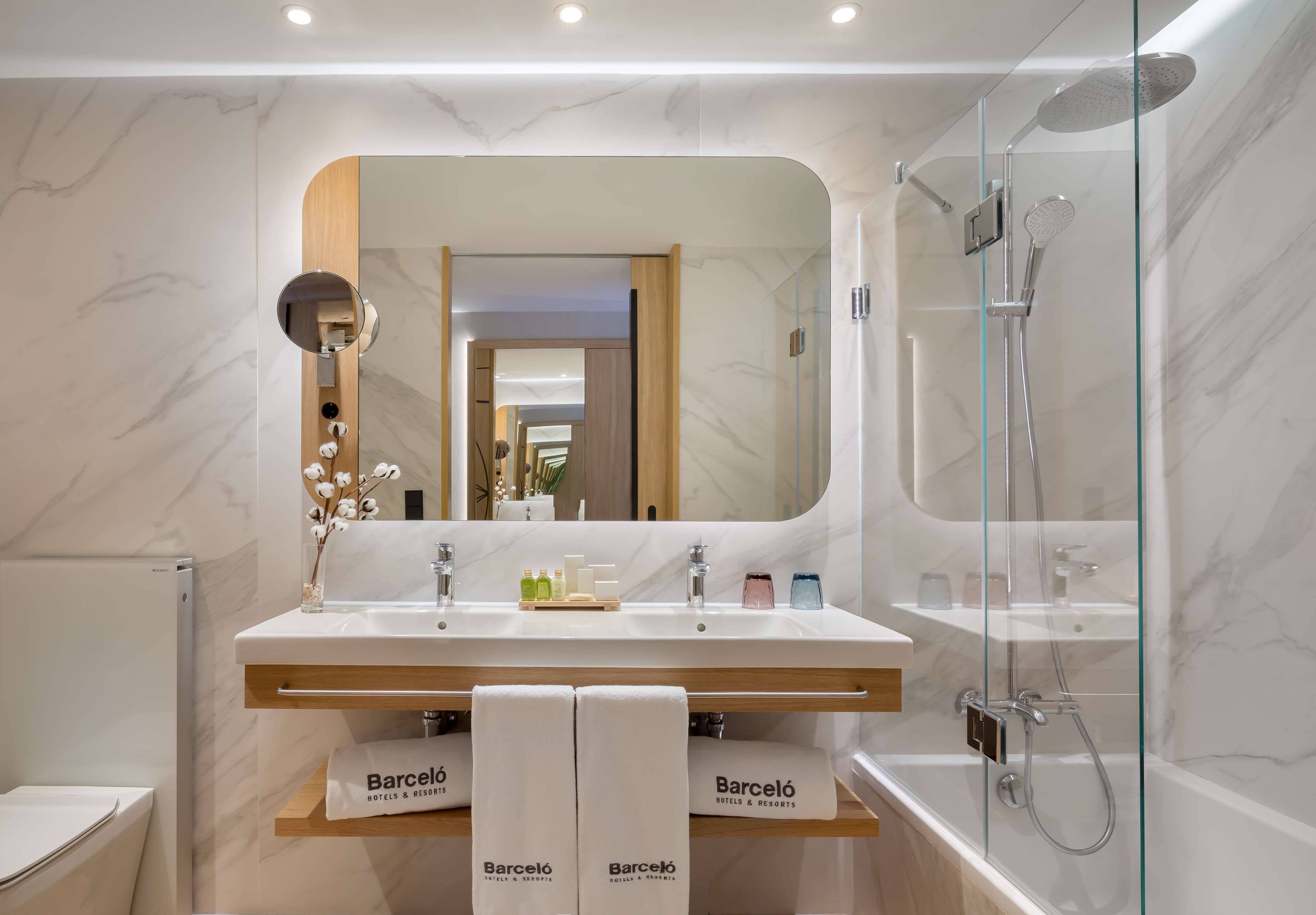 Un bany modern amb una paret de marbre, un mirall gran, un lavabo doble i una dutxa amb envà.
